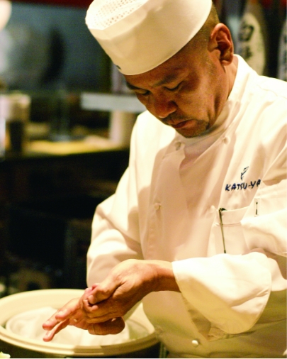 Sushi chef in a Katsu-ya uniform carefully forming a piece of sushi by hand.