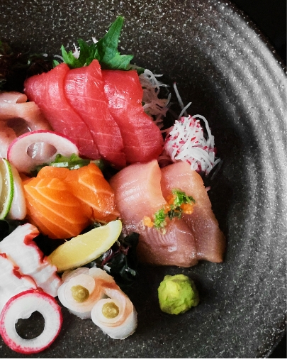 Assorted sashimi plate featuring slices of tuna, salmon, white fish, and octopus, garnished with radish, lime, and wasabi.