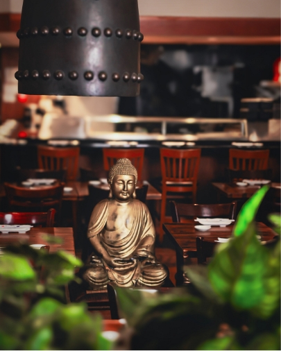 Golden Buddha statue centerpiece in a dimly lit, warm-toned Japanese restaurant dining area.