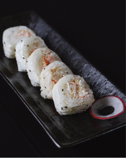 Five pieces of white sushi roll with crab and black sesame seeds, served on a dark, modern rectangular platter.